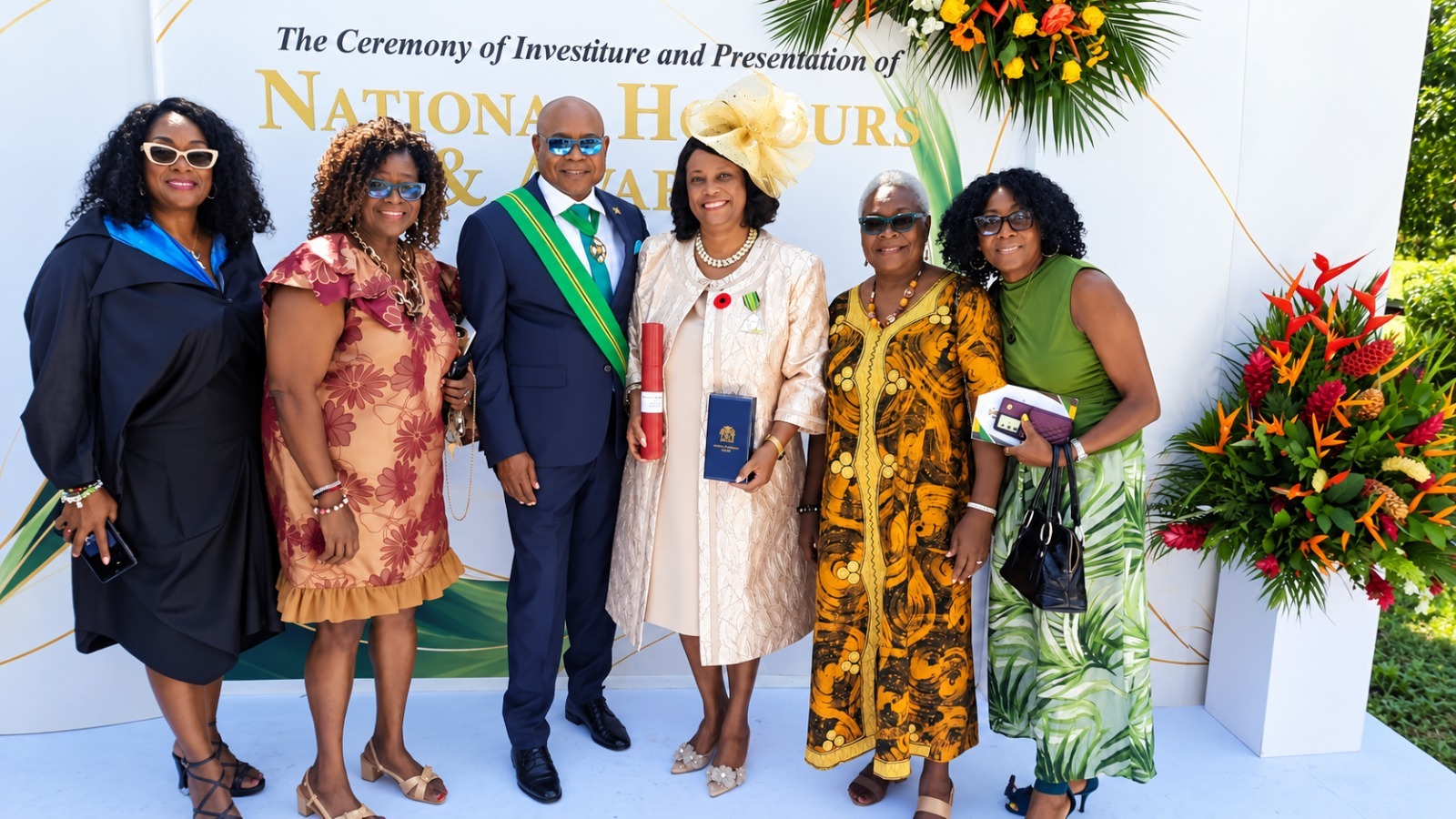 Judith James-Watts, OD and a group of guests posing at the National Honours and Awards backdrop.